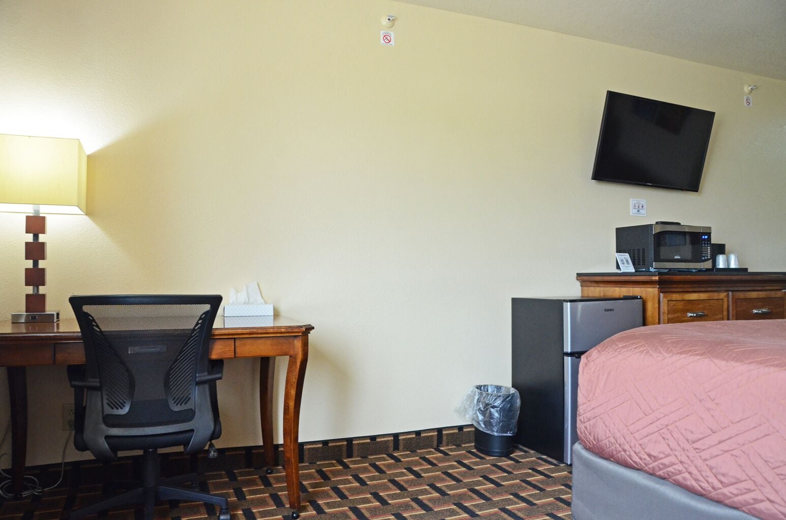 A hotel room with a desk, chair, television, microwave, refrigerator, and a bed.