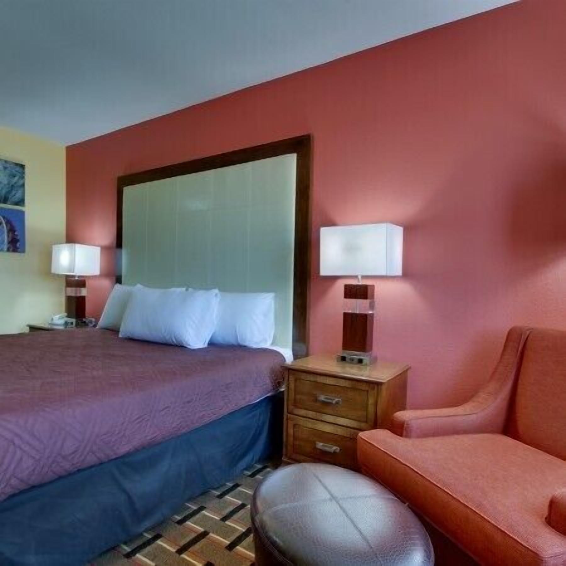 A hotel room with a bed, a nightstand, a lamp, a chair, and a small table.