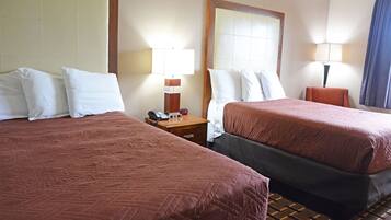 A hotel room with two beds, a nightstand with a phone and clock, and a lamp.