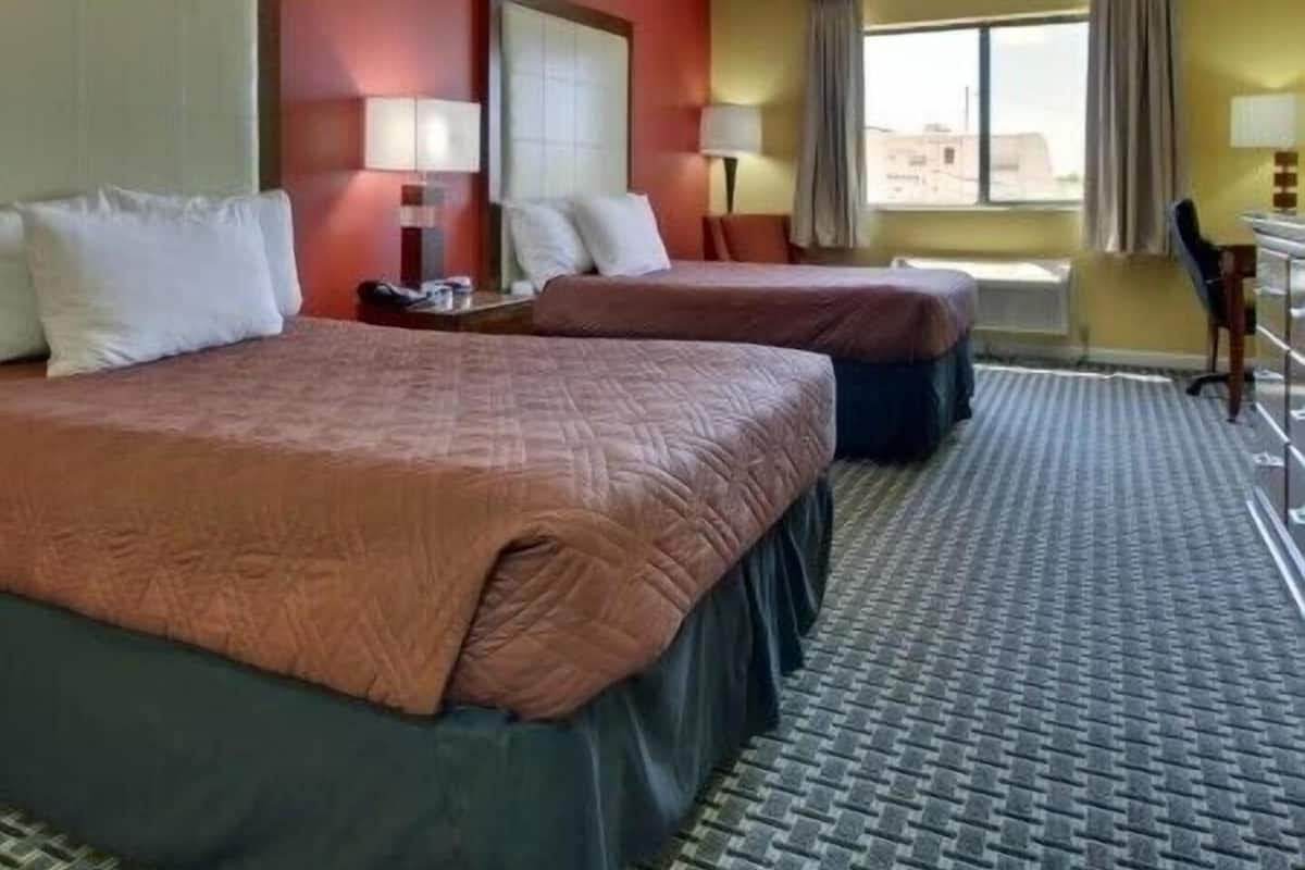 A hotel room with two beds, a desk, and a chair.