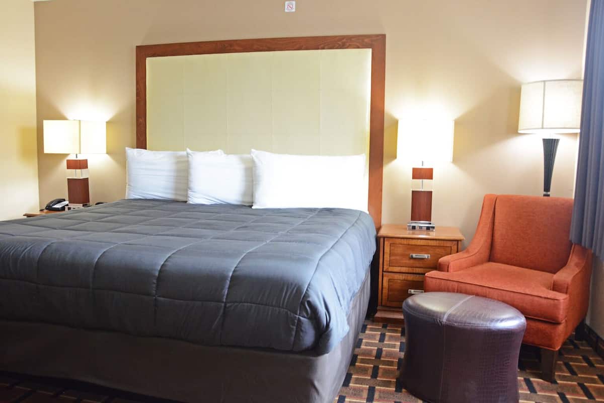 A hotel room with a large bed, two bedside tables with lamps, a chair, and a small ottoman.