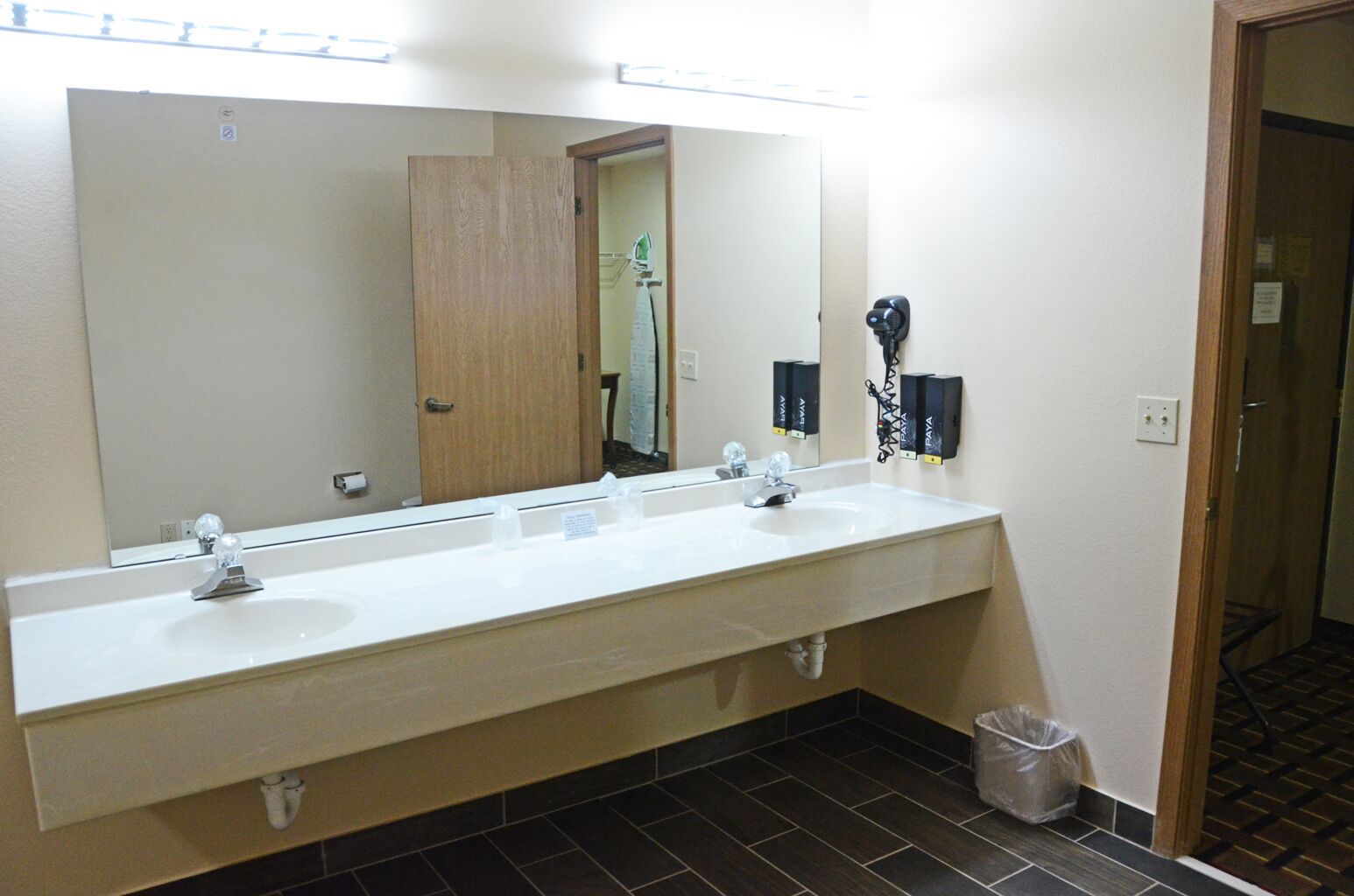 A hotel bathroom with a long vanity, two sinks, a large mirror, and a hairdryer.
