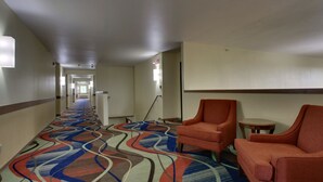 A hotel corridor with a patterned carpet, orange armchairs, and a small round table. - Heritage Grand Inn (Canton)