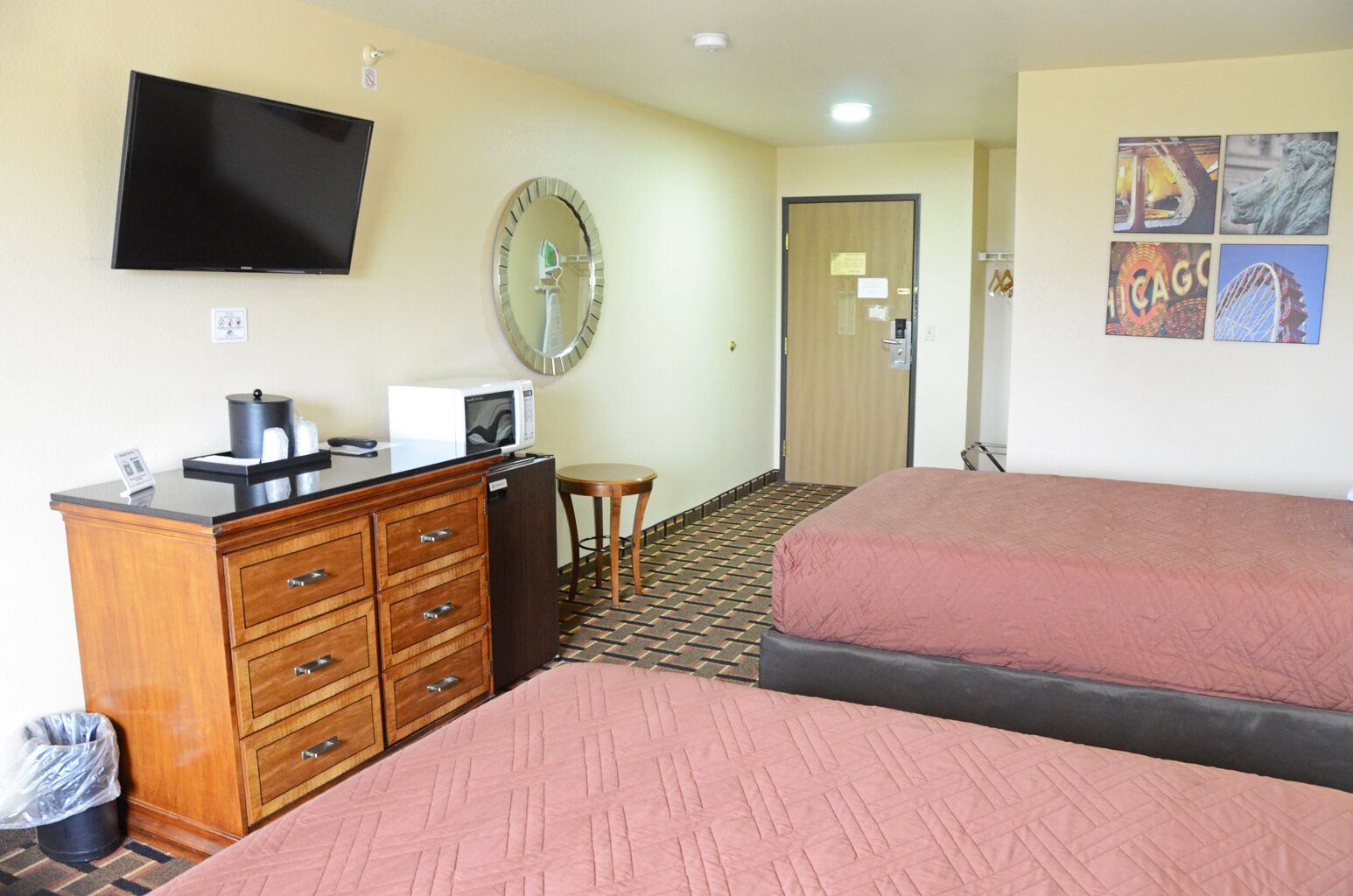 A hotel room with two beds, a desk with a computer, a television, a microwave, and a trash bin.