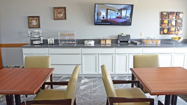A hotel room with a kitchen area, a television mounted on the wall, and a dining area with two wooden tables and chairs. - Heritage Grand Inn (Canton)