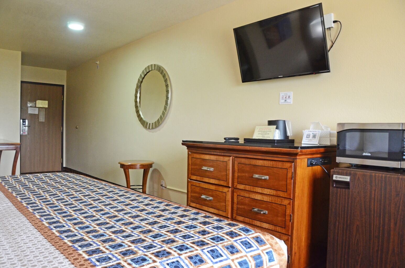Habitación de hotel con cama, cómoda de madera, microondas, televisión y una pequeña mesa redonda.