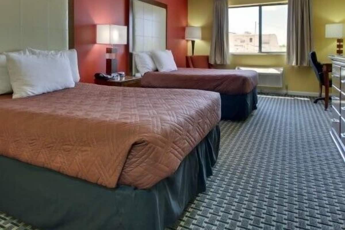 A hotel room with two beds, a desk, and a chair.