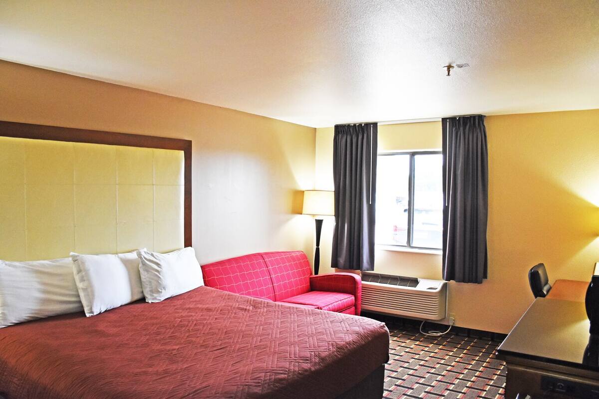 A hotel room with a large bed, a red sofa, a desk, and an air conditioning unit.