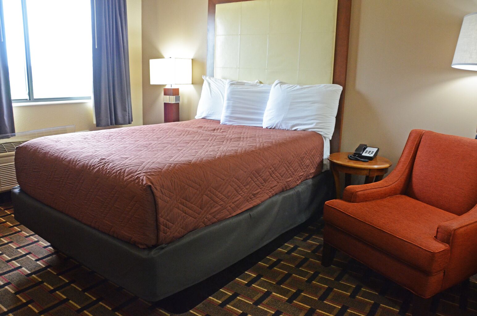 Een hotelkamer met een bed, een stoel, een lamp en een telefoon op een nachtkastje.