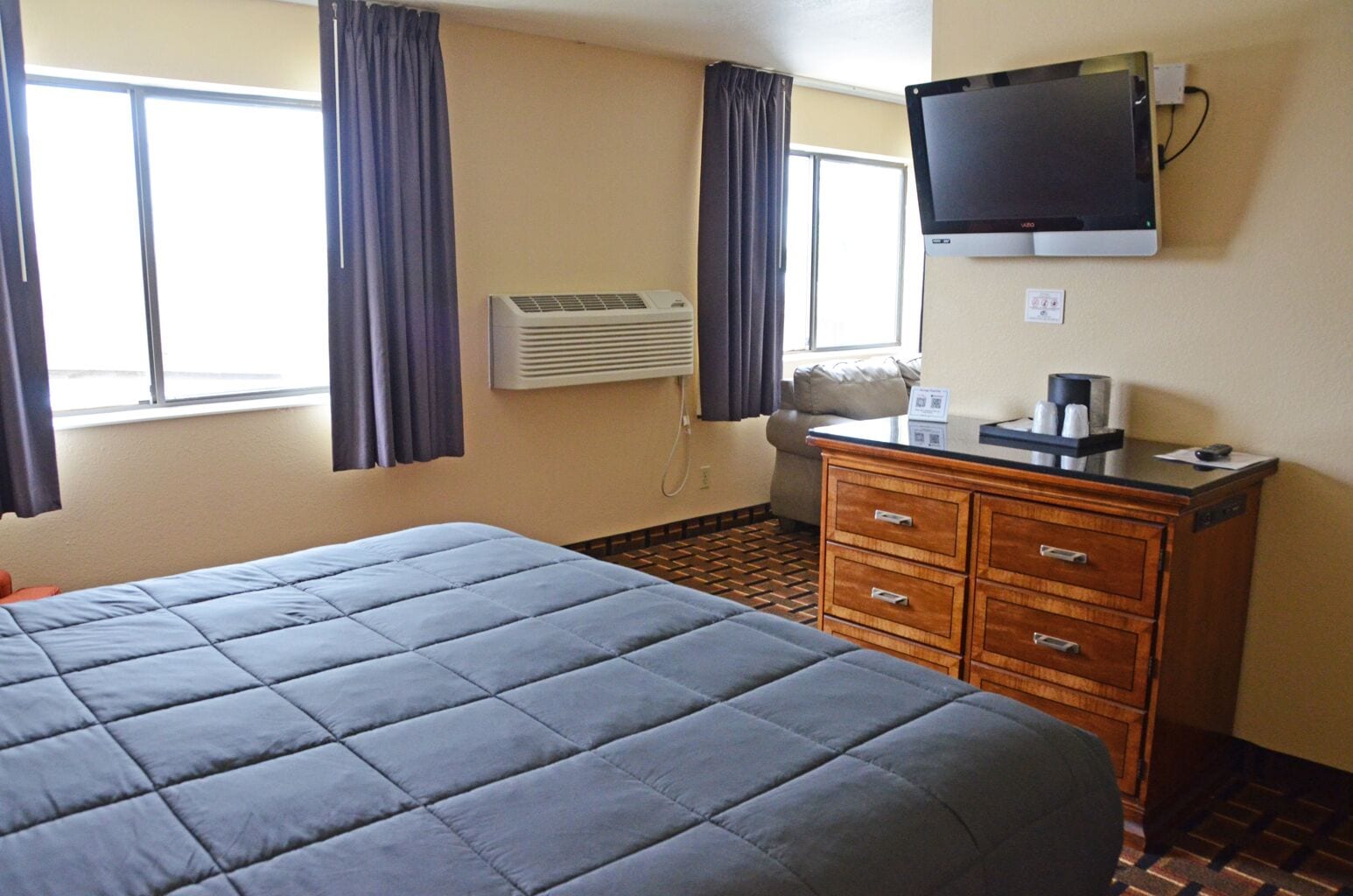 Een hotelkamer met een groot bed, een houten dressoir, een flatscreen televisie, een airconditioning en een raam met gordijnen.