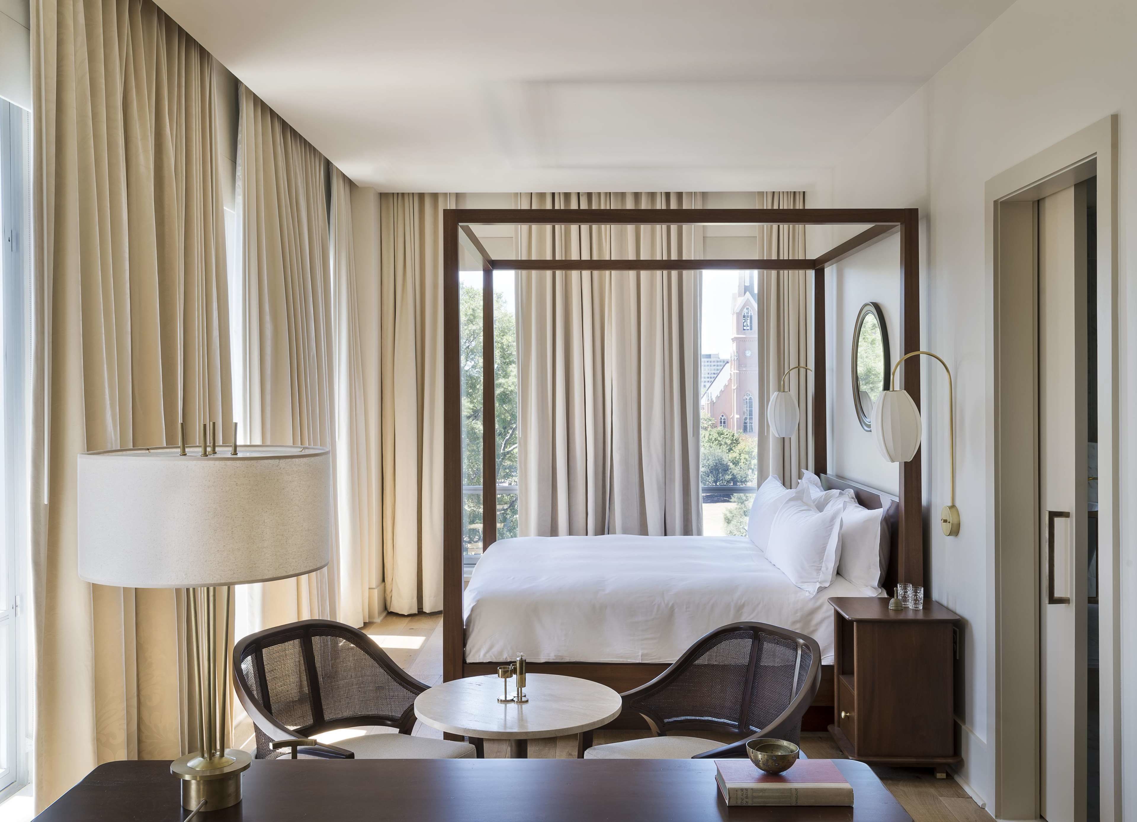 Quarto de hotel com uma cama grande, área de estar com mesa e cadeiras, luminária e mesa de cabeceira.