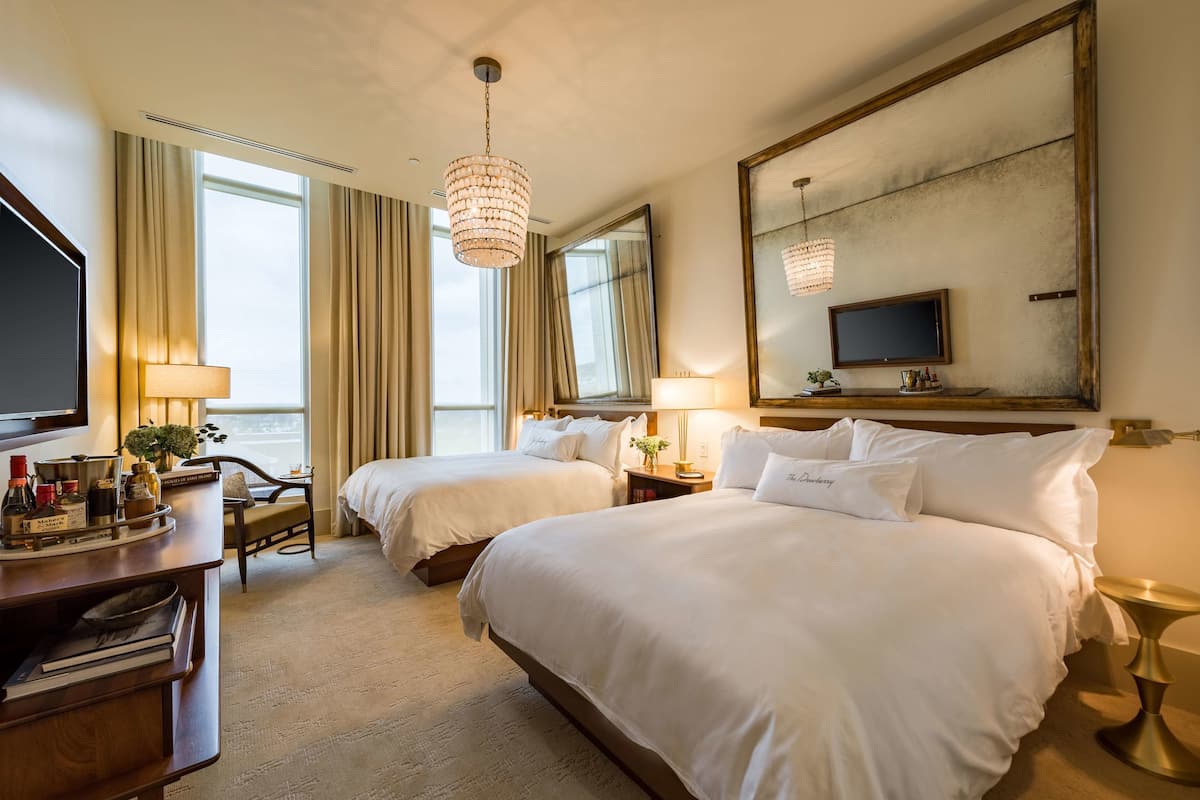 Une chambre d’hôtel avec deux lits, une télévision, un bureau avec une lampe et un grand miroir.