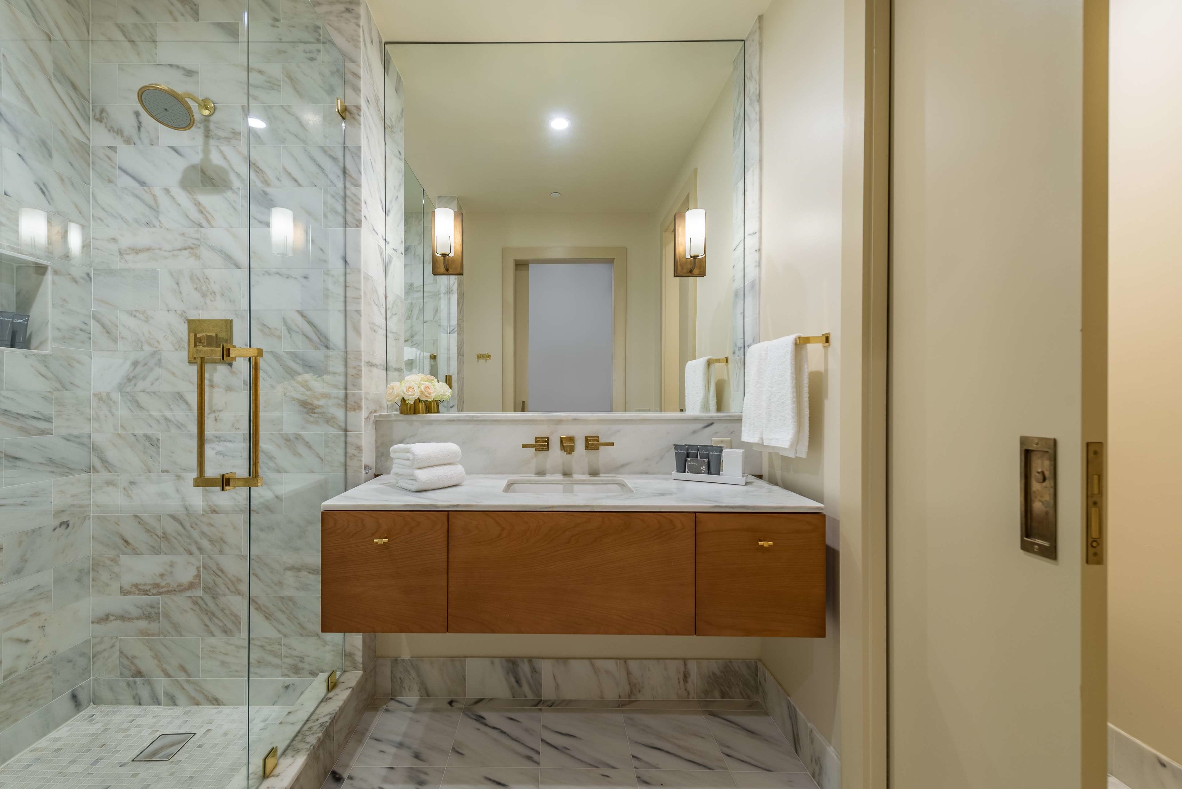 A bathroom with a marble shower, a wooden vanity with a sink, and a large mirror.