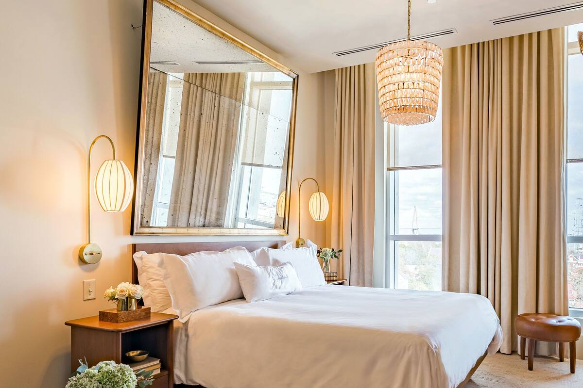 Une chambre d’hôtel moderne avec un grand lit, une table de chevet ronde, un miroir et un luminaire suspendu.