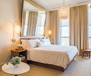 Un dormitorio de hotel moderno con una cama grande, una mesita redonda, un espejo y una lámpara colgante.