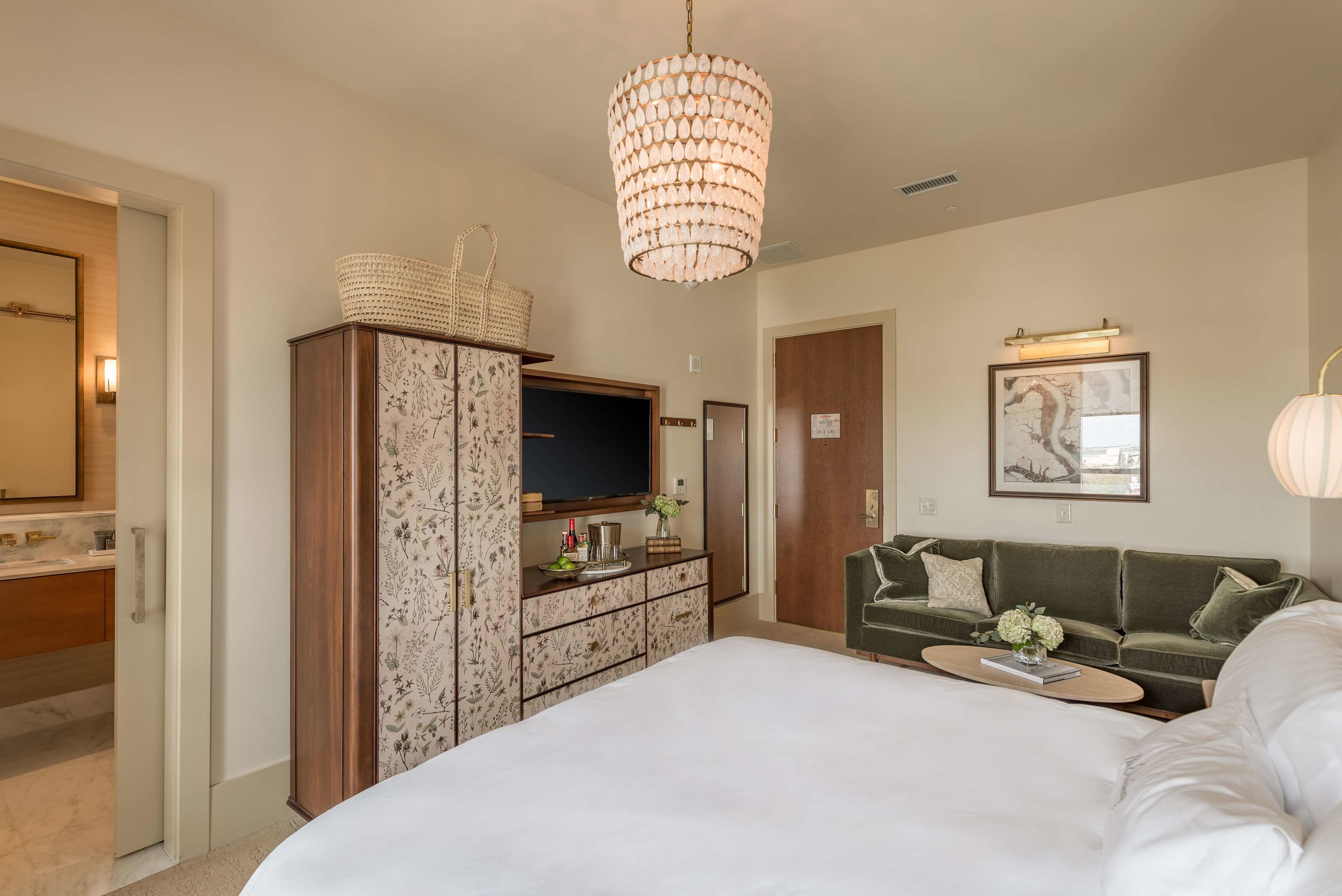 A bedroom with a large bed, a green sofa, a television on a cabinet, and a chandelier.
