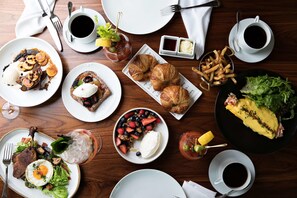 A variety of breakfast dishes including eggs, croissants, and fruits, served on a wooden table with multiple cups of coffee. - The Dewberry Charleston (Charleston)
