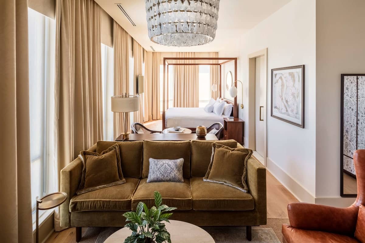 Une chambre d’hôtel avec un grand lit, un canapé, une table à manger et un lustre.