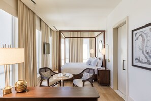 A hotel room with a bed, a desk, two chairs, a bedside table, a lamp, and a large window with curtains. - The Dewberry Charleston (Charleston)