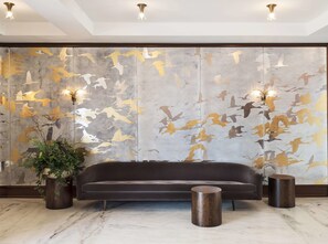 A modern living room with a dark sofa, two round wooden side tables, and a large abstract wall mural. - The Dewberry Charleston (Charleston)