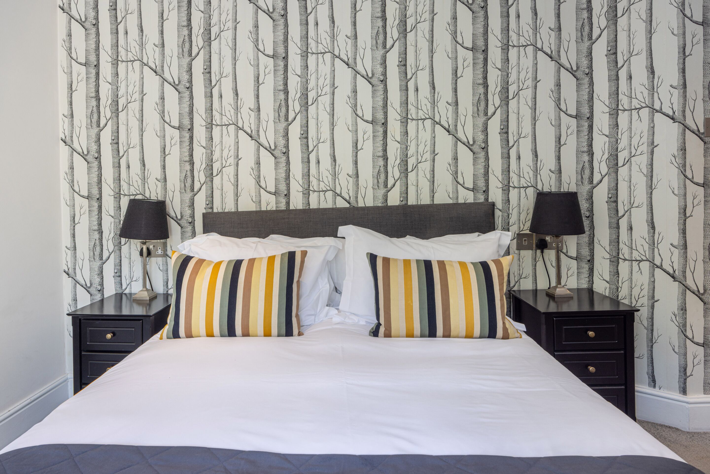 A neatly made bed with striped pillows and two bedside tables with lamps.