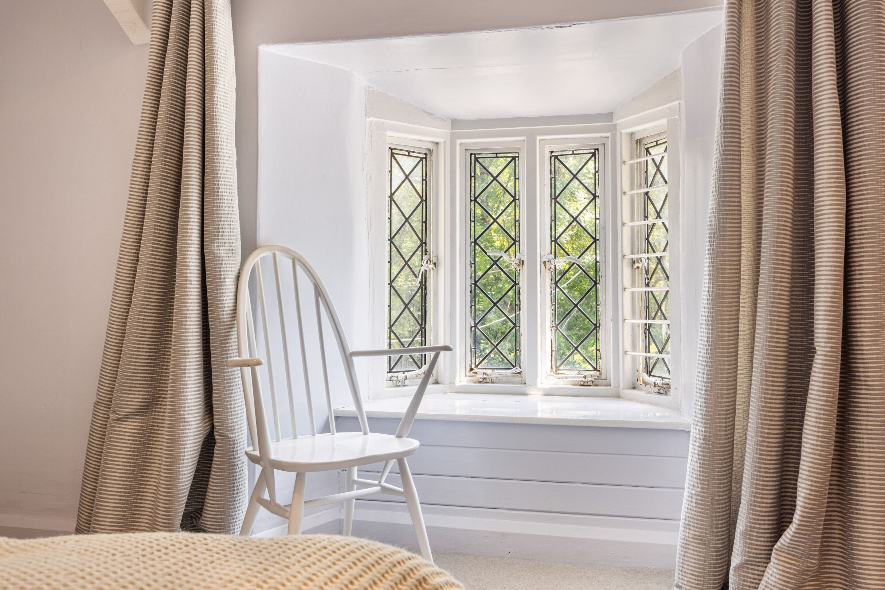 Una habitación con ventanal, una silla blanca y cortinas.