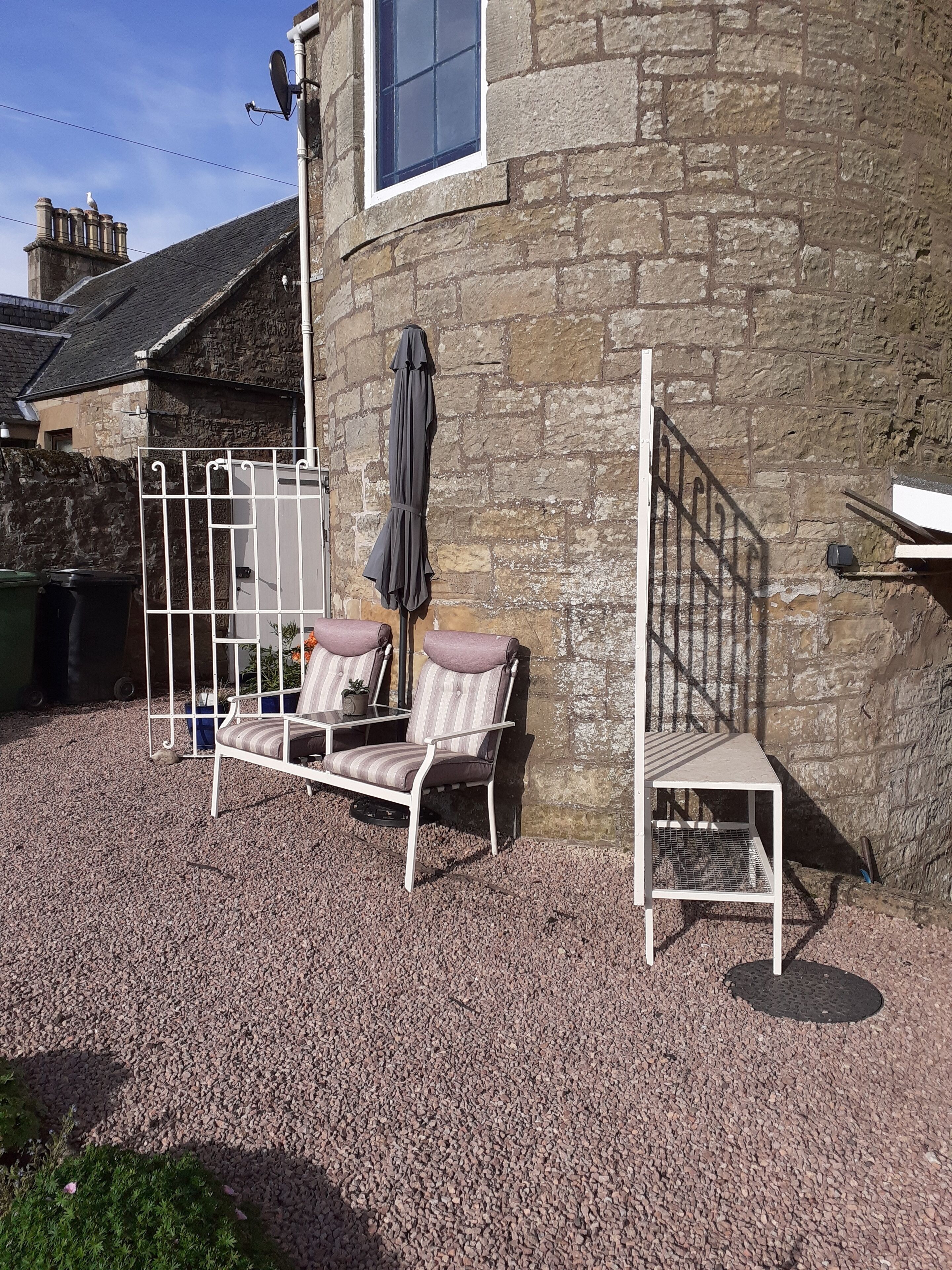 A stone building with a white metal bench and a small table in front of it.