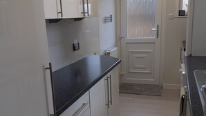 Una cocina con armarios blancos, encimera negra y una puerta con vidrio esmerilado.
