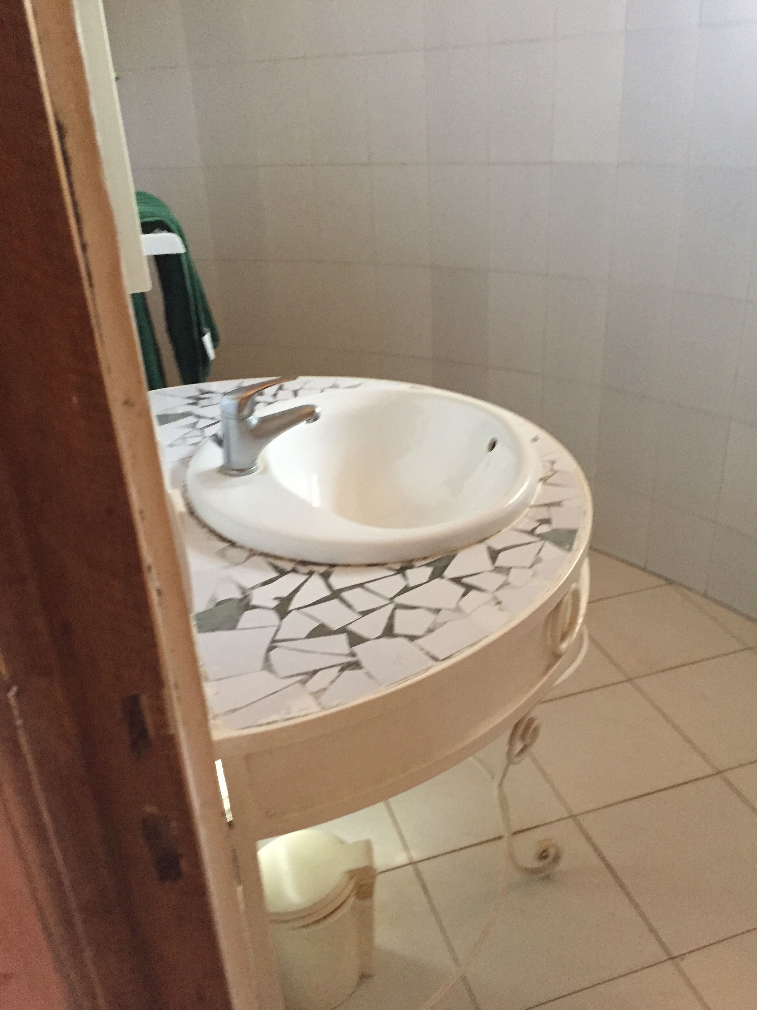 Casa de banho com lavatório branco, bancada em mosaico e chão em azulejos.