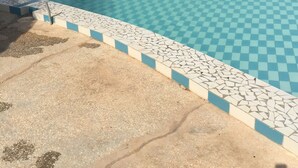 En swimmingpool med skakternet fliser, omgivet af liggestole og parasoller af strå.