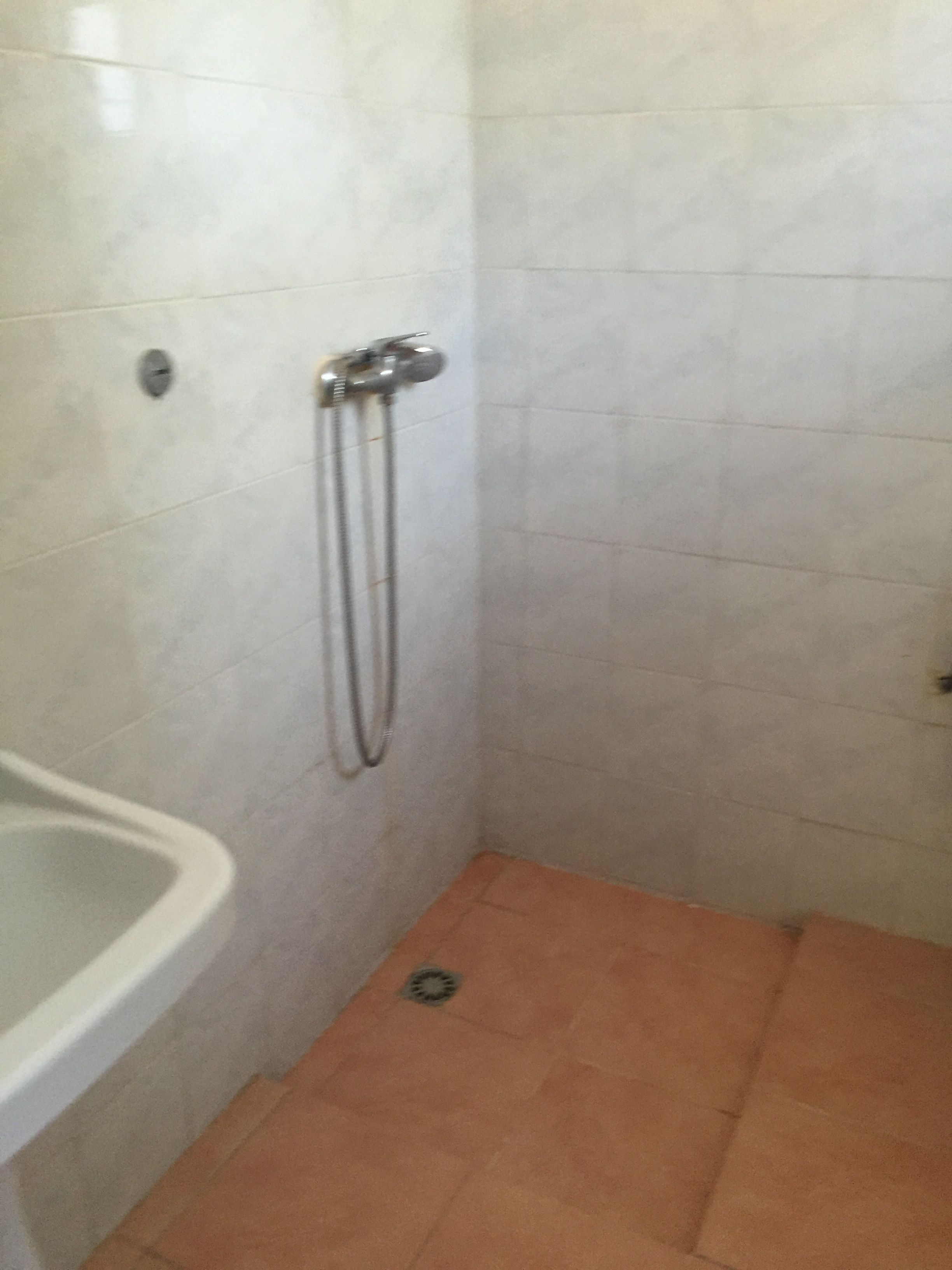 Un espacio de ducha pequeño con azulejos, un lavamanos blanco y un cabezal de ducha.