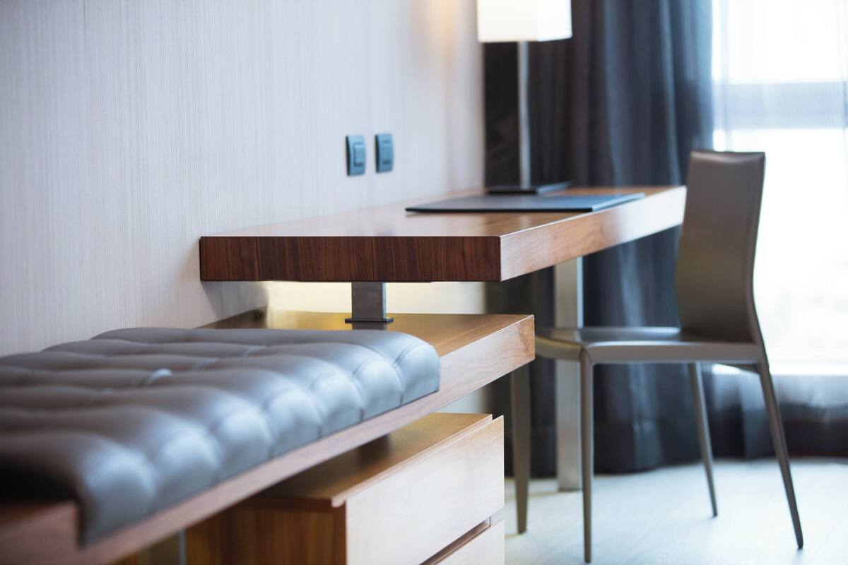 Ein modernes Hotelzimmer mit einem Holztisch, einer gepolsterten Bank, einem Sessel und einer Lampe.