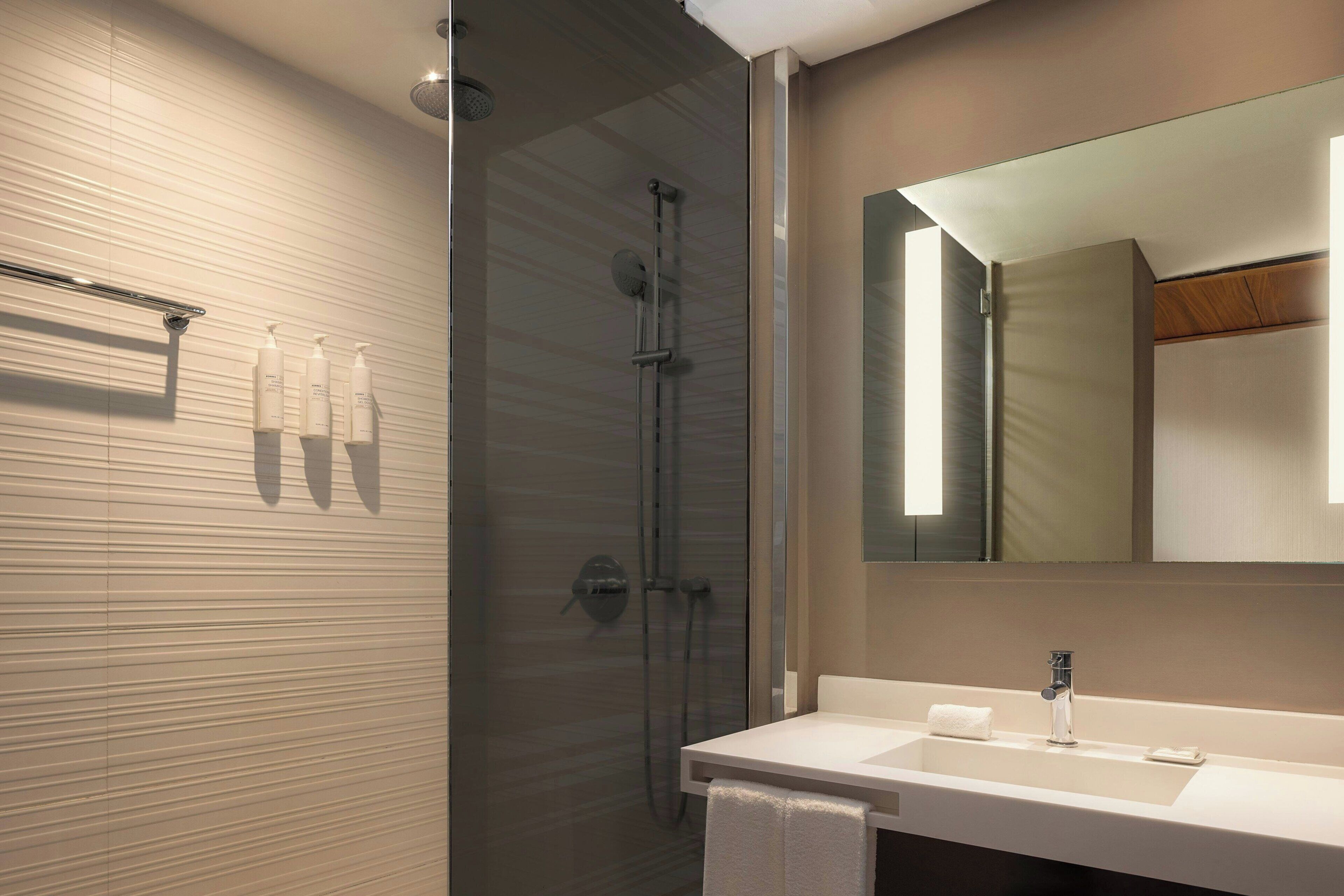 Un baño moderno con ducha de vidrio, lavamanos blanco y un espejo grande.