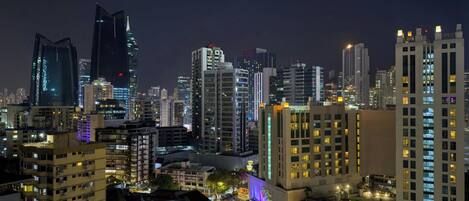 A cityscape at night with illuminated buildings, including a prominent skyscraper with a unique design.