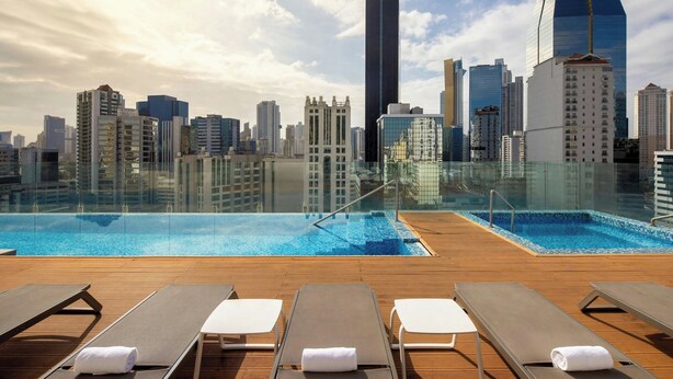 A rooftop pool with lounge chairs and a city skyline view.