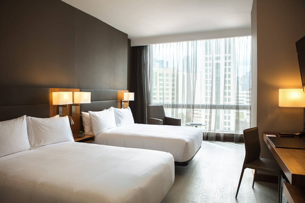A hotel room with two beds, a desk, and a chair.