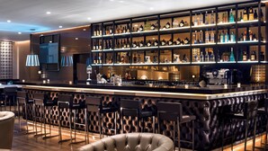 A bar area with a counter, multiple shelves of bottles, bar stools, and a tufted leather wall.