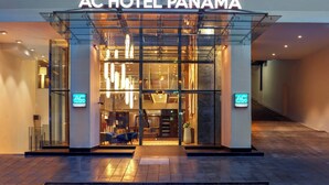 The exterior of AC Hotel Panama with a modern glass entrance, visible seating area outside, and signage indicating it is a Marriott hotel.