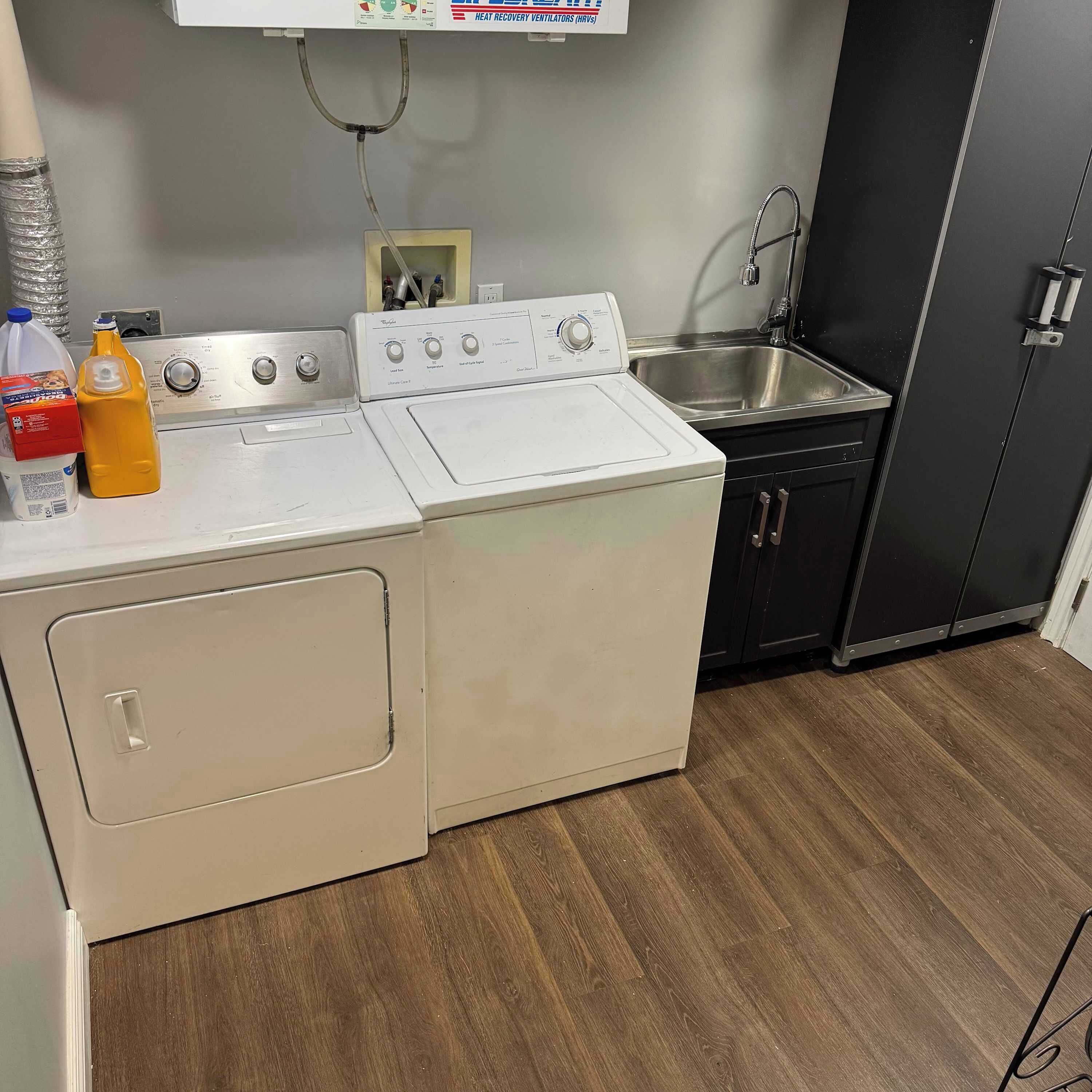 Cozinha compacta com máquina de lavar e secar, pia de aço inoxidável e armário preto.