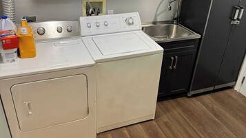 Une cuisine compacte équipée d’un lave-linge et d’un sèche-linge, d’un évier en acier inoxydable et d’un meuble noir.