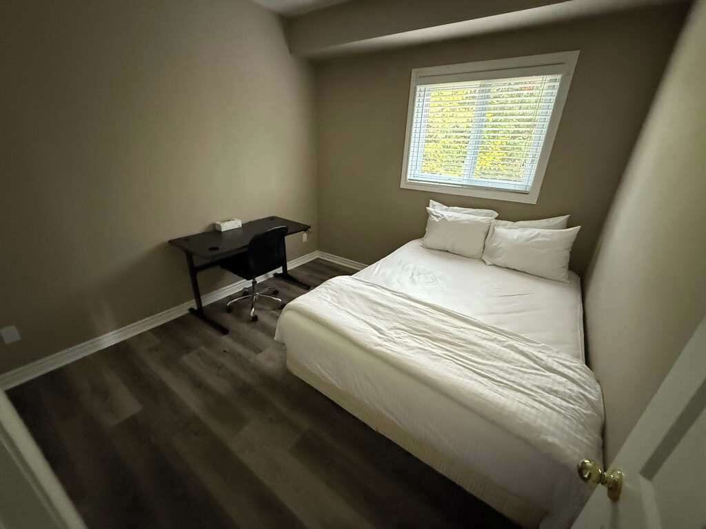 A bedroom with a bed, a desk, and a window with blinds.