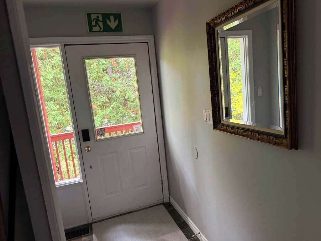 A hallway with a white door, a red railing outside, and a mirror on the wall.