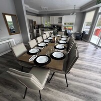Un comedor moderno con una larga mesa de madera dispuesta para una comida, rodeada de sillas cómodas.