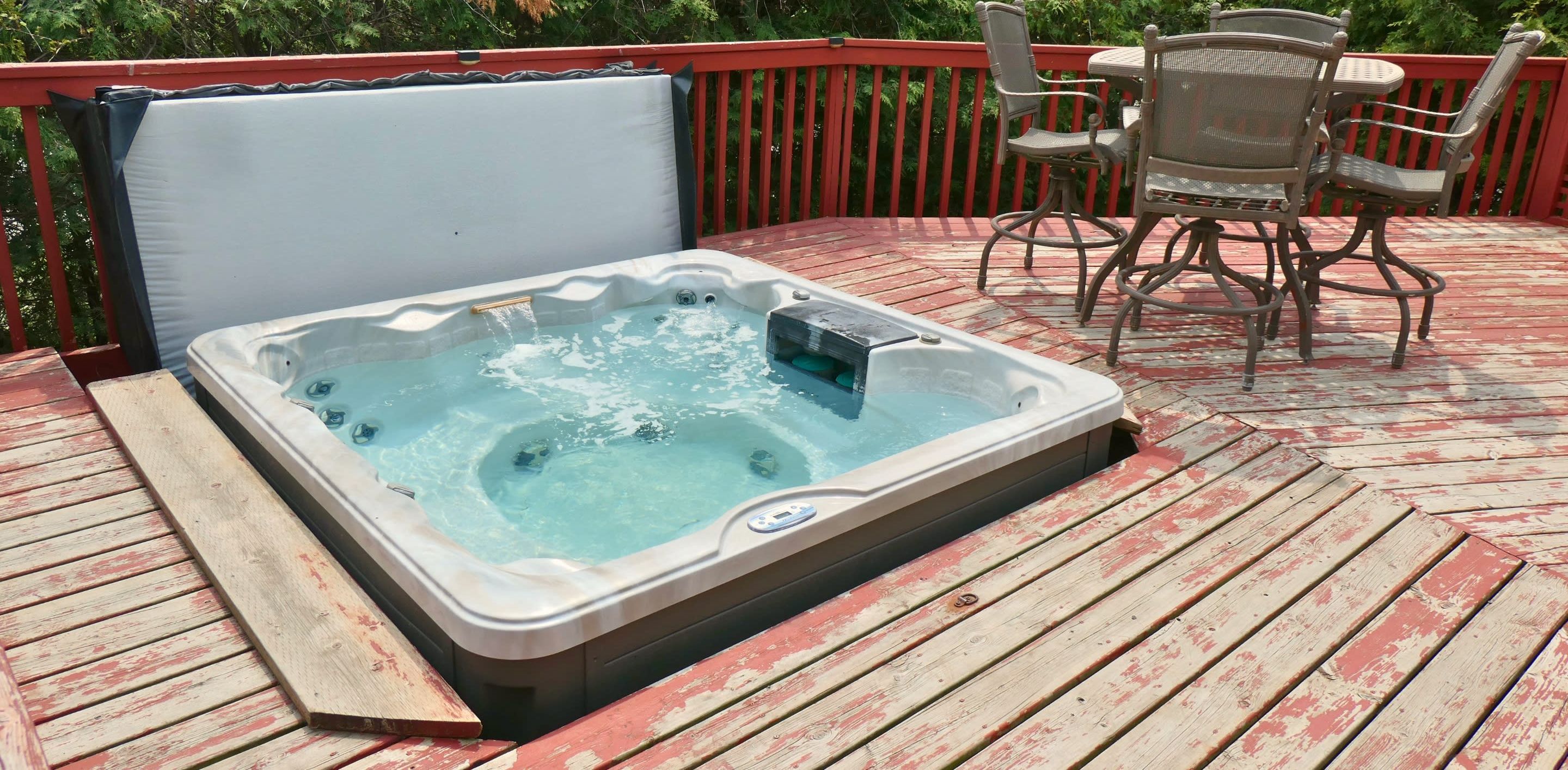 Un jacuzzi en una terraza de madera con barandilla roja, rodeado de follaje.
