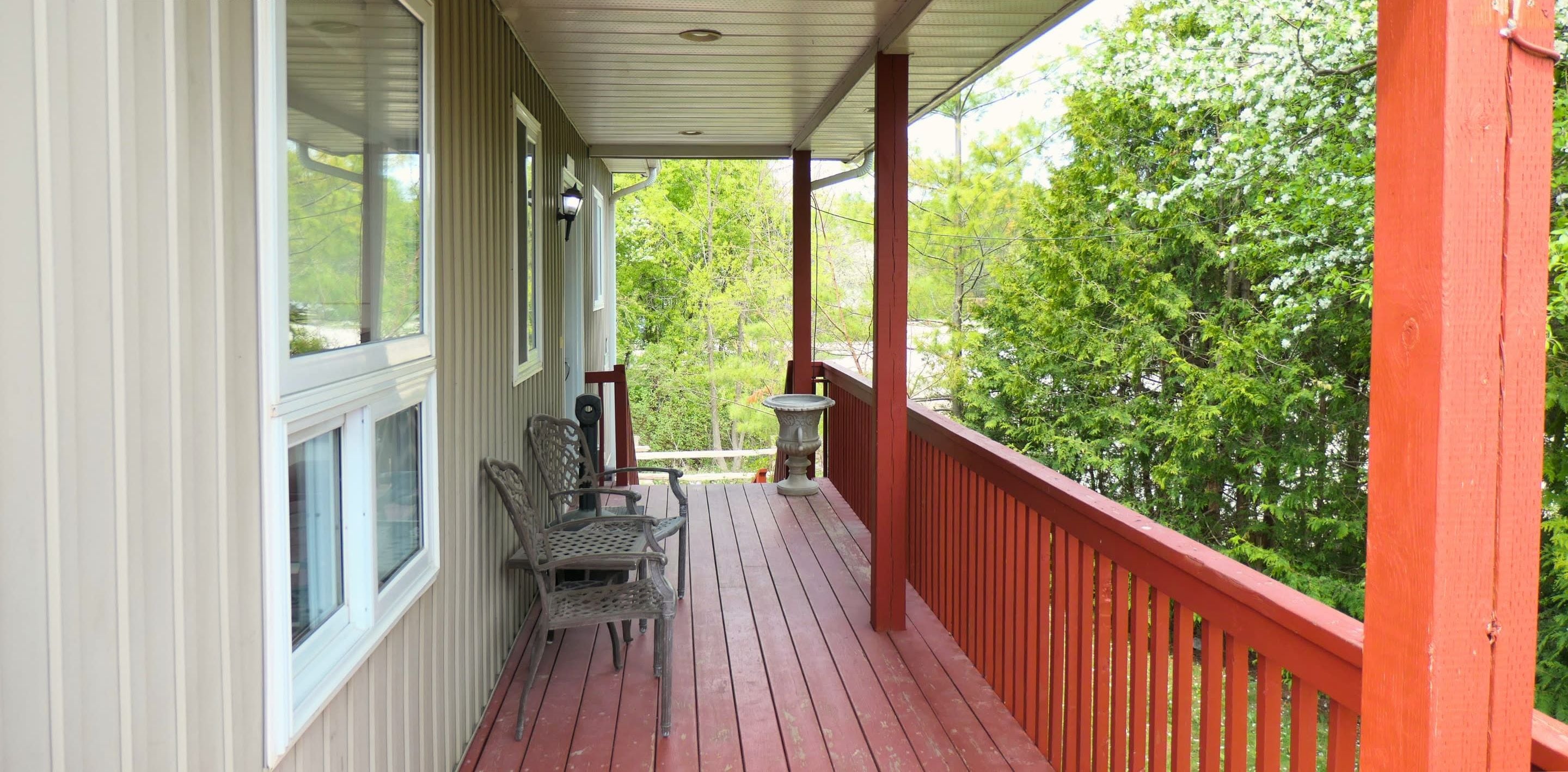 A covered porch with a red railing, a table, and two chairs.