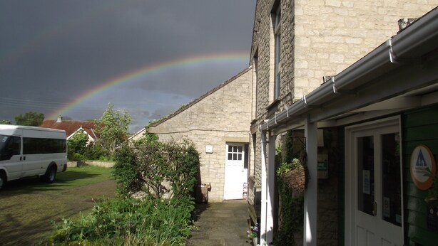 A stone building with a door and windows, a van parked in front, and a rainbow in the sky. - YHA Helmsley - Hostel (York)