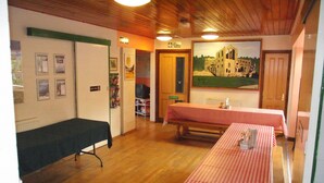 A room with wooden floors, a table with a red and white checkered tablecloth, a bench, and a painting of a building on the wall. - YHA Helmsley - Hostel (York)