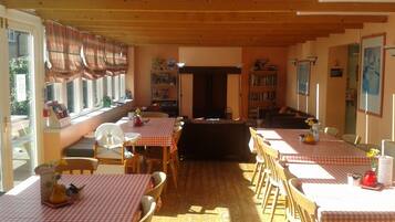 A dining area with checkered tablecloths, wooden chairs, and a bookshelf.