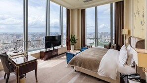 A hotel room with a large bed, a desk with a computer, a TV, and a view of a cityscape.