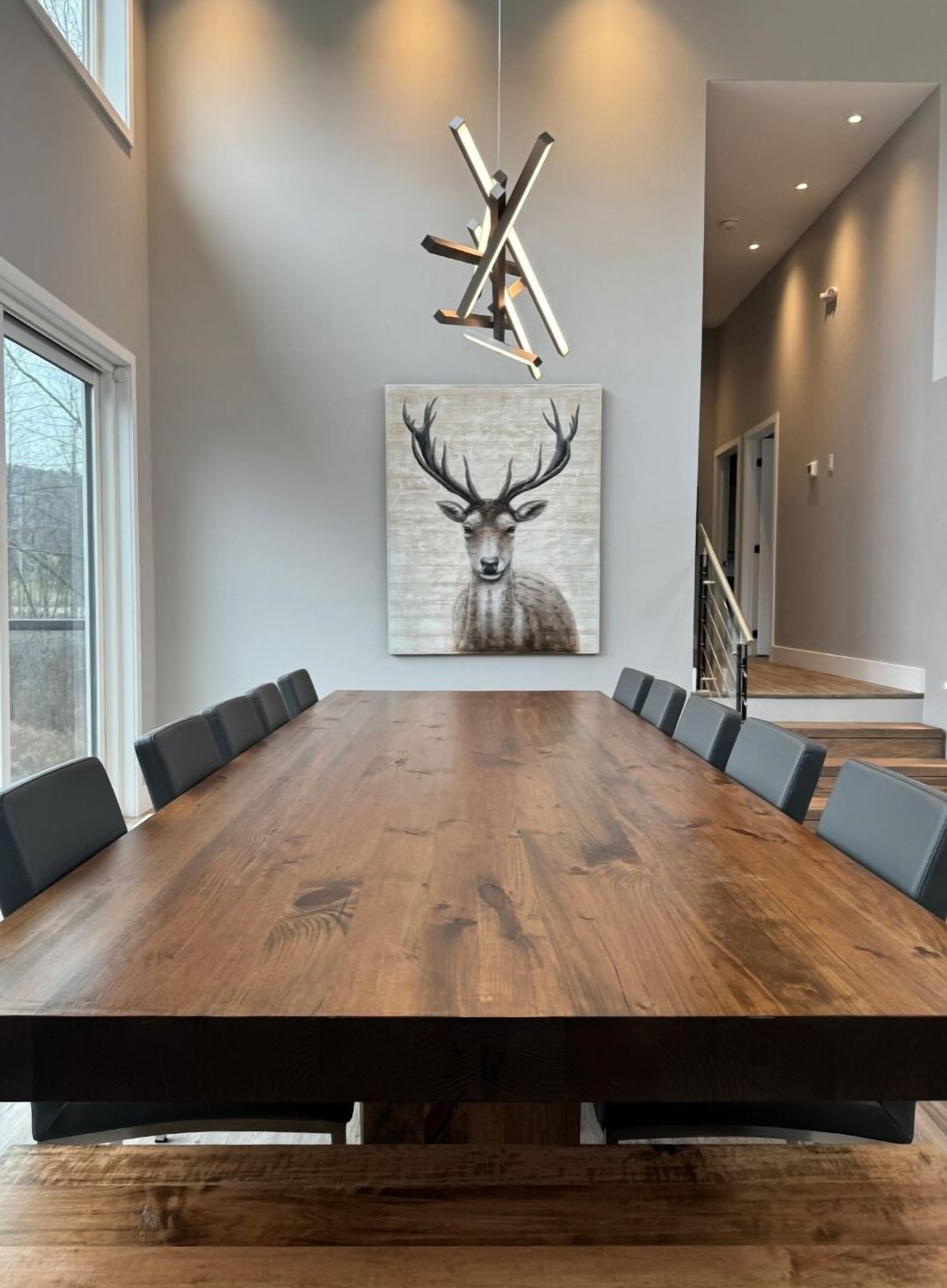 A conference room with a long wooden table, black chairs, a deer painting, and a modern light fixture.